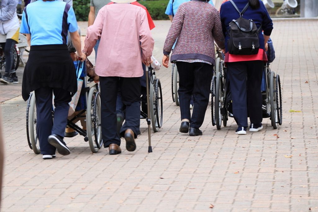 複数名の高齢者が、介護士に連れられて歩いている様子