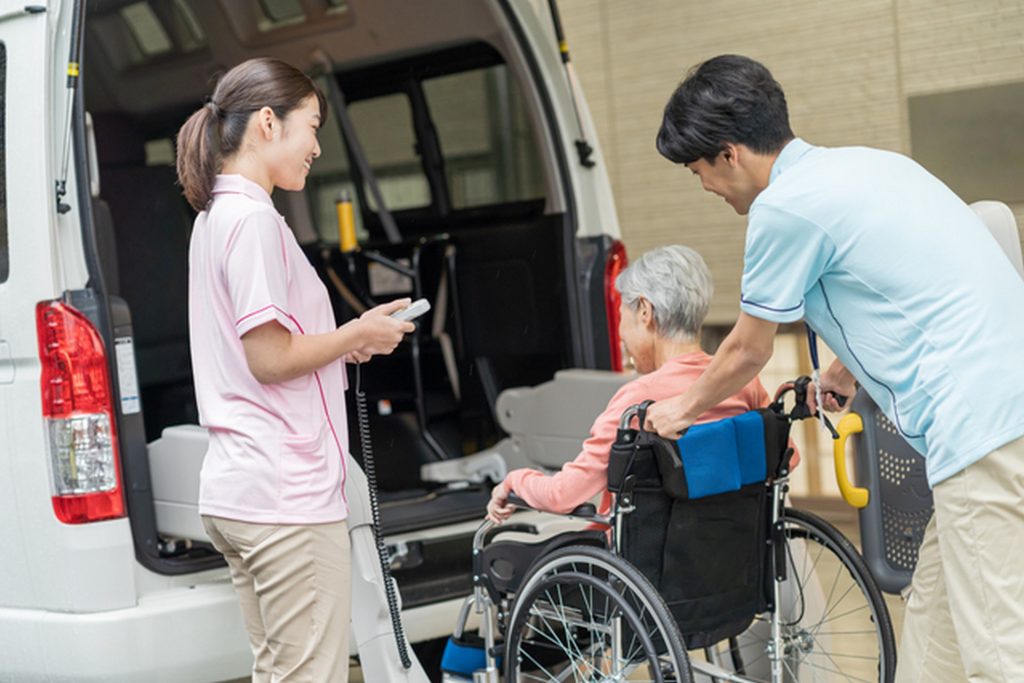 男性介護士と女性介護士が車椅子に乗っている高齢助成を介護用送迎車に乗せる様子