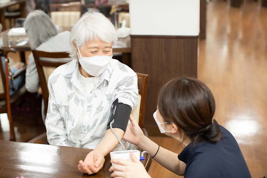 高齢女性が看護スタッフに血圧測定をされている様子